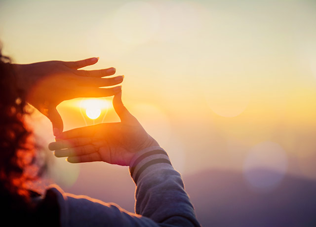 Eine Frau umrahmt mit den Händen die aufgehende Sonne