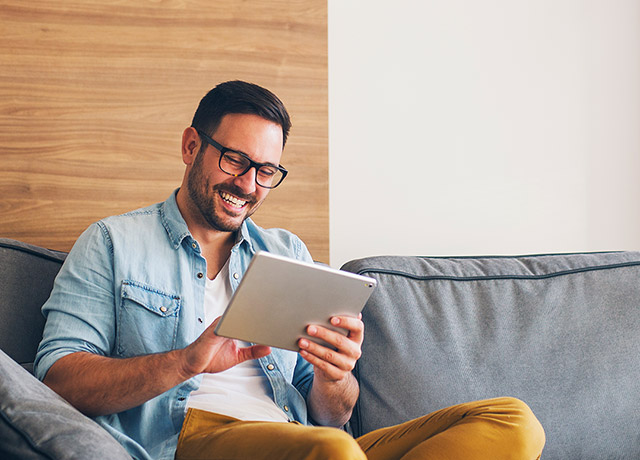 Glücklicher Mann sitzt zufrieden mit seinem tablet auf der Couch