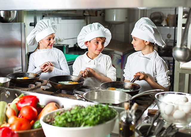 Kinder mit professionellen Kochmützen kochen mit Gas