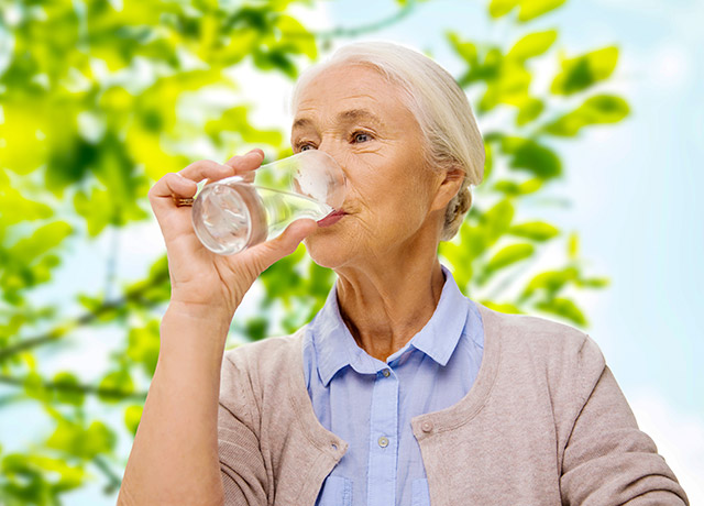 Seniorin trinkt zufrieden ein Glas klares Wasser im Freien